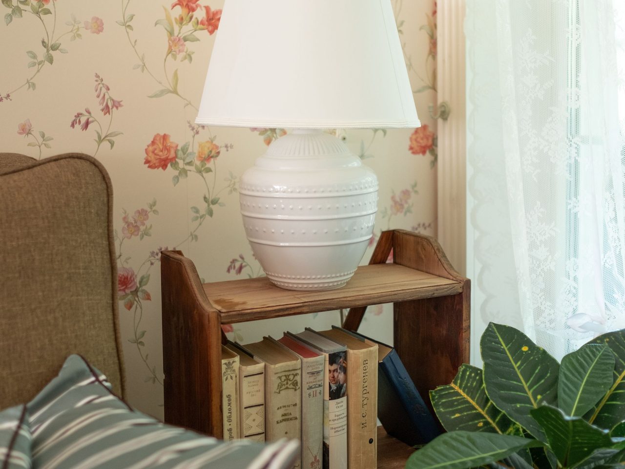 Cozy reading nook with cream rose-floral wallpaper, a wood bookshelf and a ceramic lamp