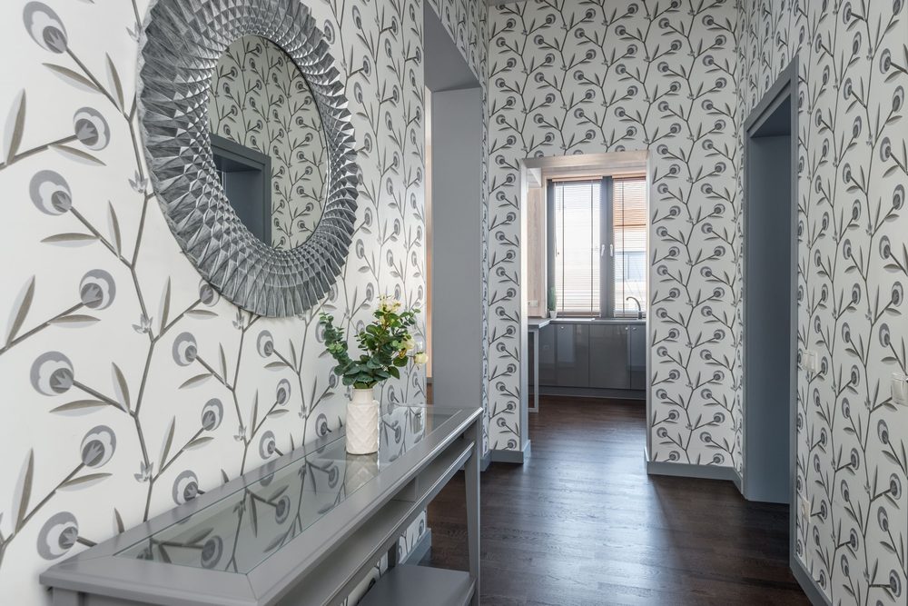 Hallway lined with blue-grey peacock-feather patterned wallpaper and a round sunburst mirror