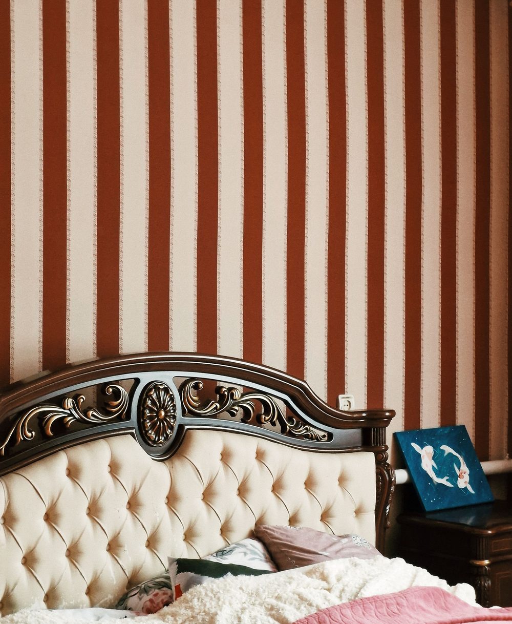 Bedroom with terracotta and cream vertical stripe wallpaper behind an ornate carved headboard