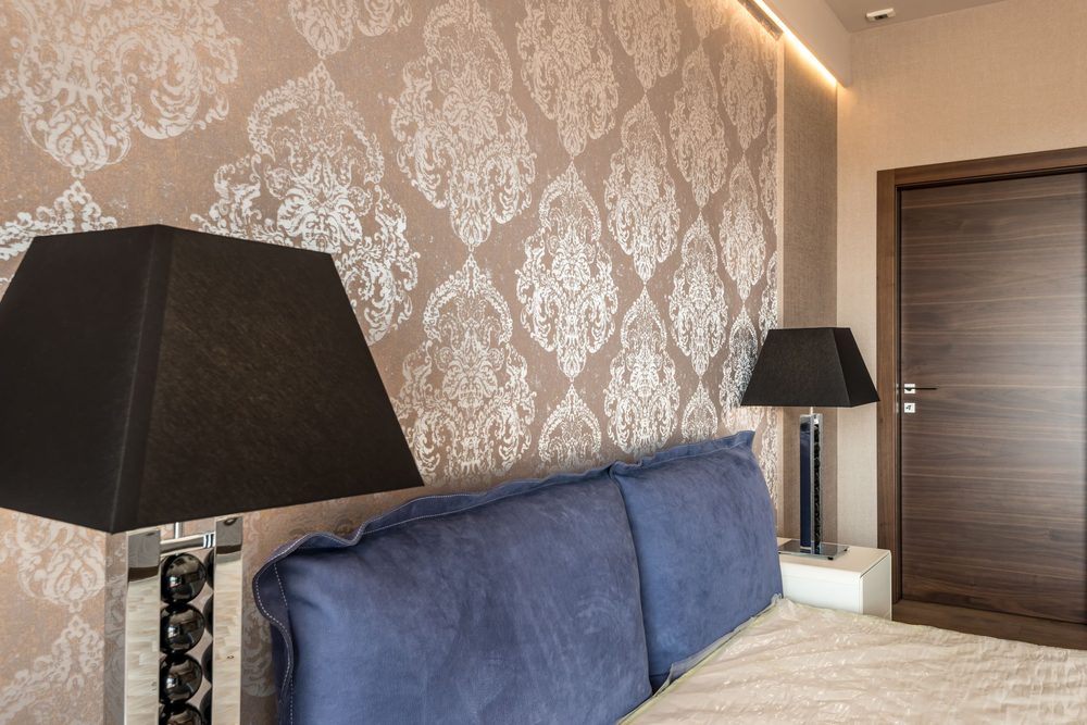 Bedroom with taupe and silver metallic damask wallpaper behind a navy upholstered headboard