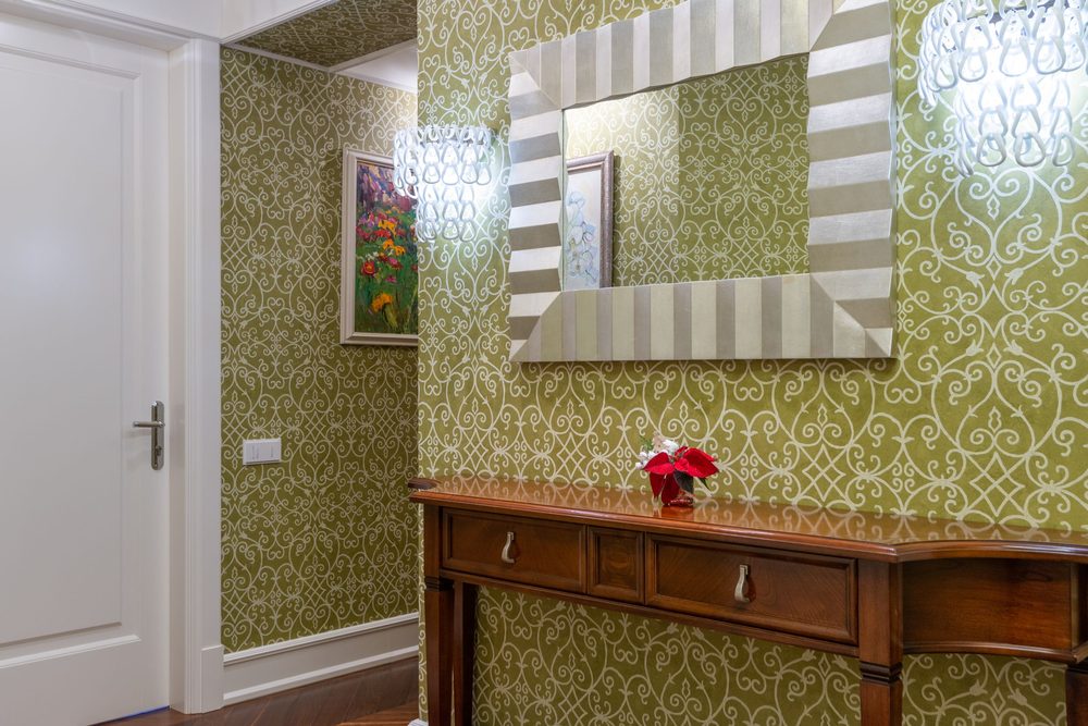 Entryway with olive-green ornate scroll damask wallpaper, a wood console and a chandelier